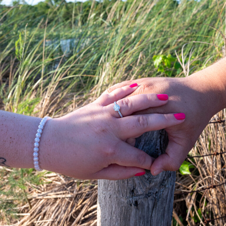 Kaylan and Joe holding hands proudly showing engagement ring during engagement session at Sandy Hook, NJ